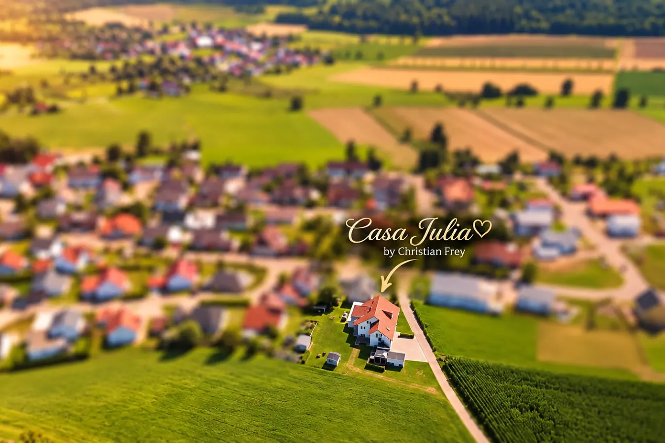 Luftaufnahme von Burgweiler: Wohnhäuser mit roten Ziegeldächern zwischen Wiesen und Feldern, ein goldener Pfeil zeigt auf das Haus der Ferienwohnung am Ortsrand.